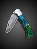 Rippled copper Damascus steel blade extended on blue and green folding knife