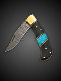 Clip point Damascus steel blade extended on brown and blue folding pocket knife