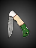 Patterned Damascus steel blade extended on green and cream folding pocket knife