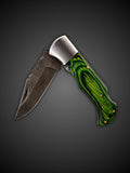 Swirling Damascus steel blade extended on green handcrafted folding pocket knife
