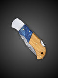 Close up of wood and blue accent handle on Lara Eagle copper Damascus pocket knife