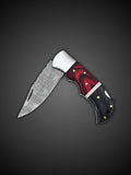 Rippled Damascus steel blade extended on red and black folding pocket knife