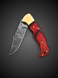 Rippled Damascus steel blade extended on red handcrafted folding pocket knife